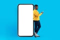 Mobile Mockup. Young Blank Man With Smartphone Standing Near Big Blank Telephone