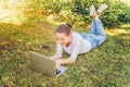 Mobile Office. Freelance business concept. Young woman lying on green grass lawn in city park working on laptop pc computer. Royalty Free Stock Photo