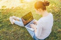 Mobile Office. Freelance business concept. Young woman sitting on green grass lawn in city park working on laptop pc computer. Royalty Free Stock Photo