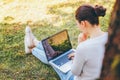 Mobile Office. Freelance business concept. Young woman sitting on green grass lawn in city park working on laptop pc computer. Royalty Free Stock Photo