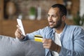 Mobile Payments Concept. Smiling Black Guy Using Smartphone And Credit Card Royalty Free Stock Photo