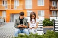 Mobile phone addiction concept - couple looking at their mobile phone while on a date sitting on the bench in city street Royalty Free Stock Photo