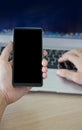 A mobile phone with a black screen in the hand of a young man Close up. The other hand typing on keyboard computer Royalty Free Stock Photo