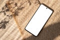 Mobile phone with blank screen mock up on sand beige jute rug background with natural floral sunlight shadows, aesthetic Royalty Free Stock Photo