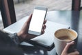 Mobile phone with blank white screen with latop and coffee cup on wooden table in cafe