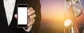 Mobile phone in businessman's hand, with satellite dish telecom network on telecommunication tower at sunrise