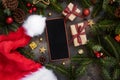 Mobile phone between Christmas decorations, Santa Claus hat, gift boxes and green fir branches Royalty Free Stock Photo