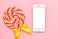 Mobile phone and colorful lolipop with wooden stick, pink, yellow and white spiral on pink background