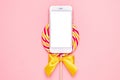 Mobile phone and colorful lolipop with wooden stick, pink, yellow and white spiral on pink background