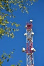 Mobile phone communication radio tv tower, mast, cell microwave antennas and transmitter against the blue sky and trees Royalty Free Stock Photo