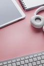 Mobile phone, computer keyboard, headphones and notebook on pink background