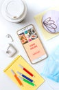 Mobile phone, donut, coffee, headphones, medical mask and materials for creativity on a white office desk. Food ordering concept.