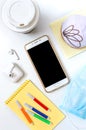 Mobile phone, donut, coffee, headphones, medical mask and materials for creativity on a white office desk. Snack dessert at the