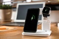 Mobile phone, earphones and smartwatch charging with wireless pad on wooden desk. Modern workplace device Royalty Free Stock Photo