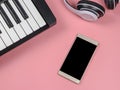 Mobile phone, electric piano and headphones on pink background with copy space, online piano lesson concept