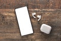 Mobile phone with empty screen and tws earphones on rustic wooden table. Wireless earphones, mobile phone. top view. copy space Royalty Free Stock Photo