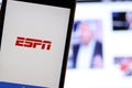 Mobile phone with ESPN logo on screen close up with website on laptop. Blurred background with ESPN Sports News.