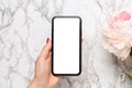 Mobile phone in in female hand with piony flowers on a marble background, using technology concept for the holidays - Valentine`s Royalty Free Stock Photo