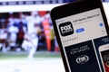 Mobile phone with Fox Sports : Watch Live logo on screen close up with website on laptop. Blurred background.