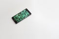 Mobile phone with green leaves on screen on white background. Royalty Free Stock Photo