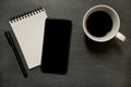 Mobile phone, gridded noted pad and cup of coffee - on dark slate