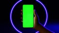 Mobile phone in hand. Holding smartphone with blue neon lighting on dark background. Green chromakey screen with markers