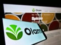 Mobile phone with logo of agribusiness company Olam International Limited on screen in front of web page.