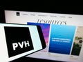 Mobile phone with logo of American clothing company PVH Corp. on screen in front of business website.