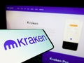 Mobile phone with logo of American crypto company Payward Inc. (Kraken) on screen in front of website.