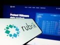 Mobile phone with logo of American data security company Rubrik Inc. on screen in front of website.