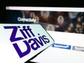 Mobile phone with logo of American digital media company Ziff Davis Inc. on screen in front of website.
