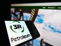 Mobile phone with logo of Brazilian oil and gas company 3R Petroleum S.A. on screen in front of web page.