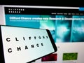 Mobile phone with logo of British law firm Clifford Chance LLP on screen in front of business website.