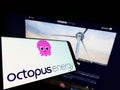 Mobile phone with logo of British renewables company Octopus Energy Group on screen in front of website.