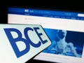 Mobile phone with logo of Canadian telecommunications company BCE Inc. on screen in front of business website.