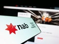 Mobile phone with logo of company National Australia Bank Limited (NAB) on screen in front of website.