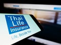 Mobile phone with logo of company Thai Life Insurance Public Co. Ltd. on screen in front of business website.