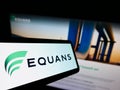 Mobile phone with logo of French facility management company EQUANS on screen in front of business website.