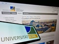 Mobile phone with logo of German education institution University of Bonn on screen in front of website.