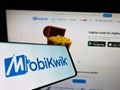 Mobile phone with logo of Indian financial technology company MobiKwik on screen in front of website.