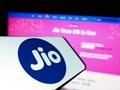 Mobile phone with logo of Indian telecommunications company Reliance Jio on screen in front of website.