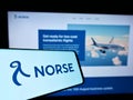 Mobile phone with logo of Norwegian airline Norse Atlantic Airways on screen in front of company website.