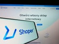 Mobile phone with logo of Polish software company Shoper S.A. on screen in front of business website.