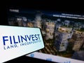 Mobile phone with logo of real estate company Filinvest Land Inc. (FLI) on screen in front of website.