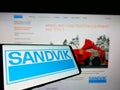 Mobile phone with logo of Swedish engineering company Sandvik AB on screen in front of business website.