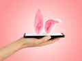 Mobile phone is lying on female palm, Easter Bunny ears sticking out of smartphone screen. Soft pink background. Happy