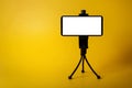 Mobile phone mounted on mini tripod with blank screen isolated on yellow background. copy space