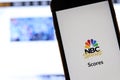 Mobile phone with NBC Sports Scores logo on screen close up with website on laptop. Blurred background with NBC news. Royalty Free Stock Photo