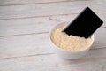 A mobile phone placed to dry in a bowl full of rice after the phone fell into water. Light wooden table background Royalty Free Stock Photo