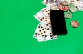 Mobile phone and poker chips with playing cards on a green table. online casino concept.